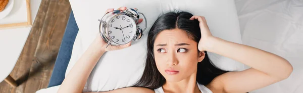 Horizontal colheita de triste asiático mulher segurando despertador na cama na manhã — Fotografia de Stock