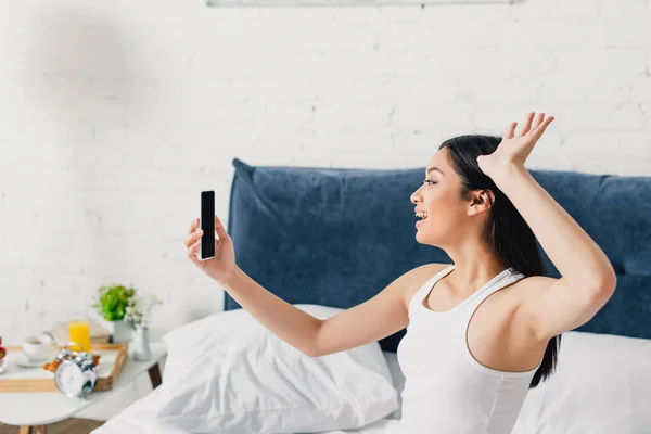 Cheerful asian girl waving hand during video call on smartphone — Stock Photo