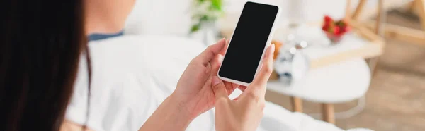 Recadrage horizontal de femme tenant smartphone avec écran blanc sur le lit — Photo de stock