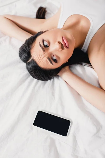 Top vista de triste mulher asiática olhando para smartphone com tela em branco na cama — Fotografia de Stock