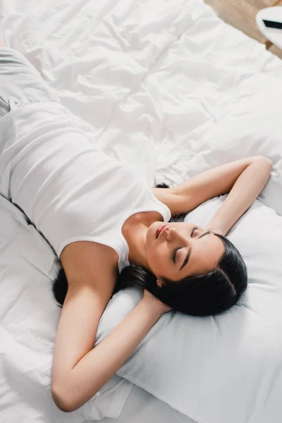 Alto angolo di vista della giovane donna asiatica in camicia senza maniche dormire sul letto al mattino — Foto stock