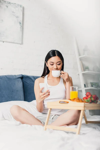 Selective focus of asian girl using smartphone during breakfast on bed — Stock Photo