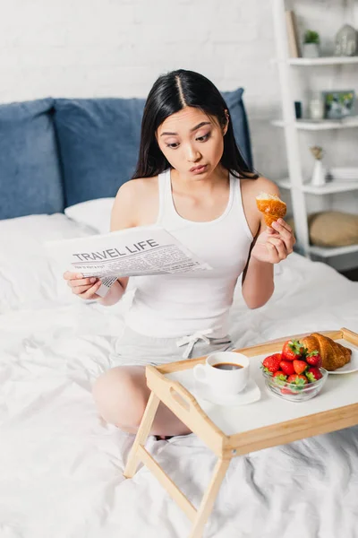 Enfoque selectivo de la mujer asiática leyendo periódico y desayunando en la cama en casa - foto de stock