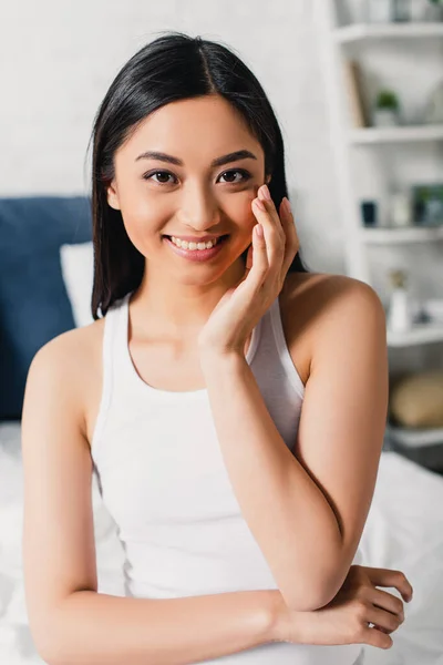 Jeune femme asiatique souriant à la caméra sur le lit — Photo de stock