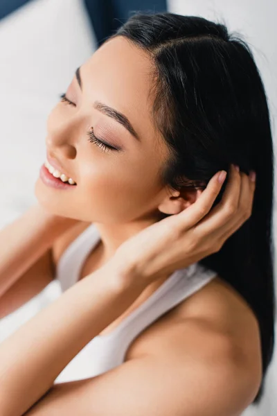 Alto ángulo vista de hermosa chica asiática sonriendo mientras toca el pelo en casa - foto de stock