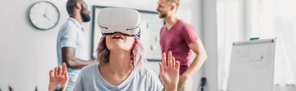 Panoramic crop of businesswoman using vr headset with multicultural colleagues at background in office — Stock Photo