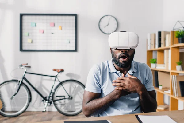 Focus sélectif d'un homme d'affaires afro-américain excité utilisant un casque de réalité virtuelle à table au bureau — Photo de stock