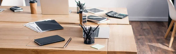 Tiro panorâmico de artigos de papelaria e dispositivos digitais em mesas no escritório — Fotografia de Stock
