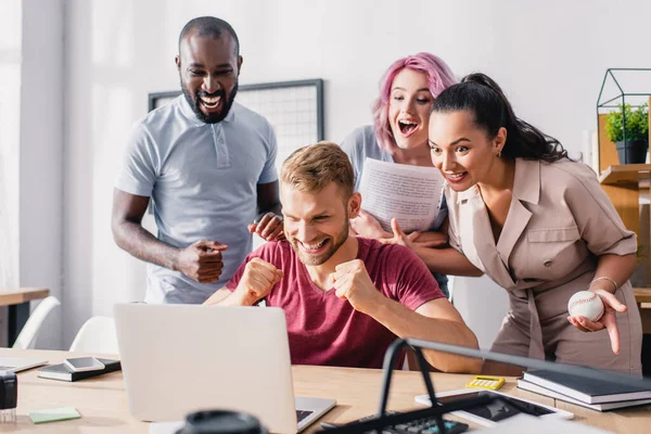 Selektiver Fokus multiethnischer Geschäftsleute, die yeah-Geste zeigen, während sie im Büro auf Laptop schauen — Stockfoto