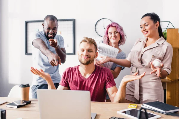 Focus selettivo di uomini d'affari multietnici che puntano al collega mostrando gesto scrollata di spalle in ufficio — Foto stock