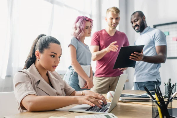 Focus selettivo della donna d'affari che utilizza il computer portatile mentre i colleghi multiculturali lavorano con appunti in ufficio — Foto stock