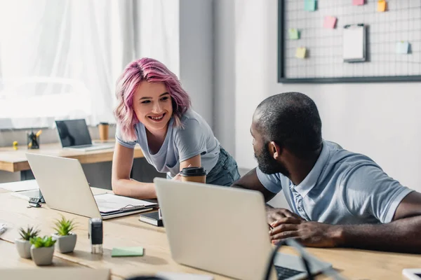 Selective focus of businesswoman holding coffee to go near african american colleague in office — Stock Photo