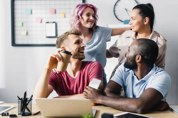 Selective focus of businesswomen embracing near multiethnic colleagues in office — Stock Photo