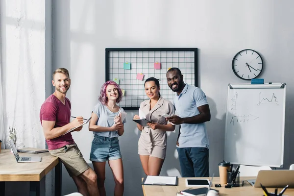 Enfoque selectivo de las personas de negocios multiétnicos mirando a la cámara mientras trabajan en la oficina - foto de stock