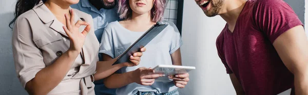 Horizontal image of businesswoman with clipboard showing ok gesture near multiethnic colleagues — Stock Photo