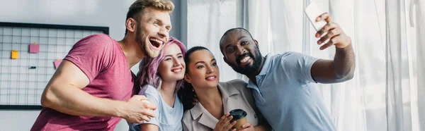 Imagen horizontal de gente de negocios multiétnicos tomando selfie con smartphone en la oficina - foto de stock