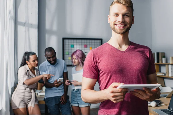 Selective focus of businessman holding digital tablet with multicultural colleagues at background in office — Stock Photo