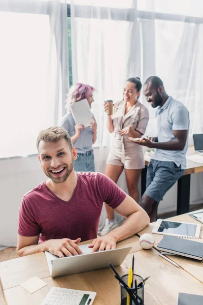 Selective focus of businessman using laptop while working near multicultural coworkers in office — Stock Photo