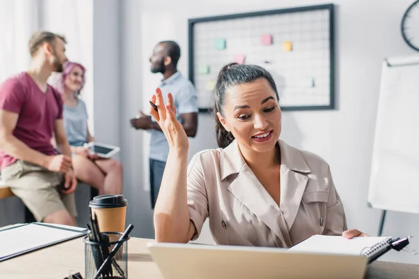 Selective focus of businesswoman holding clipboard and pen while working near colleagues in office — Stock Photo