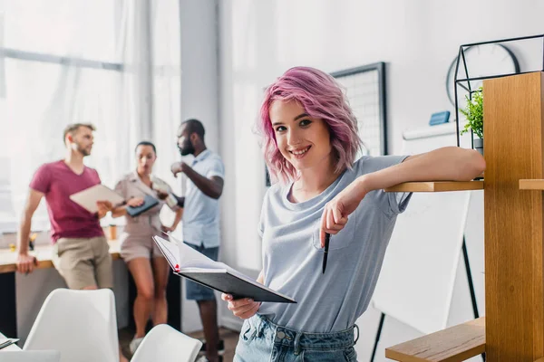 Selektiver Fokus der Geschäftsfrau, die Stift und Notizbuch in der Hand hält, während sie im Büro neben dem Schrank steht — Stockfoto