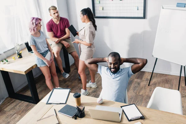 Vista de ángulo alto de hombre de negocios afroamericano mirando portátil cerca de béisbol bola anuncio café para ir a la mesa - foto de stock