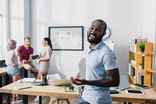 Selektiver Fokus junger afrikanisch-amerikanischer Geschäftsmann mit Baseballball und Blick in die Kamera im Büro — Stockfoto