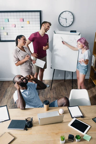 Vue en angle élevé de la femme d'affaires pointant vers le tableau blanc près des gens d'affaires multiculturels au bureau — Photo de stock