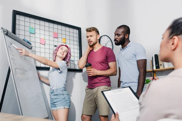 Selective focus of businesswoman pointing at whiteboard to pensive multiethnic colleagues in office — Stock Photo