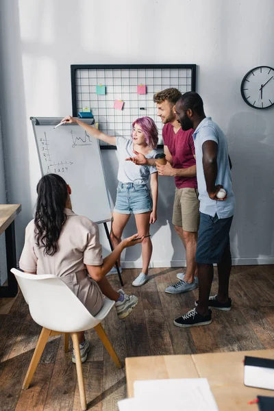 Enfoque selectivo de las personas de negocios multiétnicos que trabajan cerca de pizarra blanca con gráficos en la oficina - foto de stock