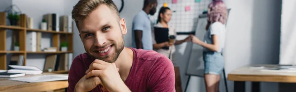 Panoramic shot of businessman looking at camera with multiethnic business people at background in office — Stock Photo