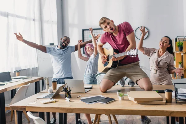 Selective focus of multicultural business people with acoustic guitar dancing in office — Stock Photo