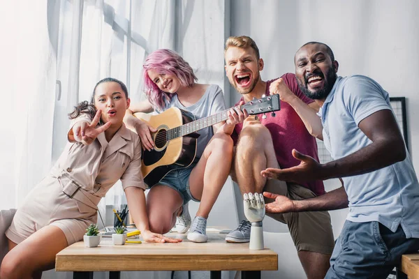 Gente de negocios multicultural con guitarra acústica mostrando gesto de paz en la oficina - foto de stock