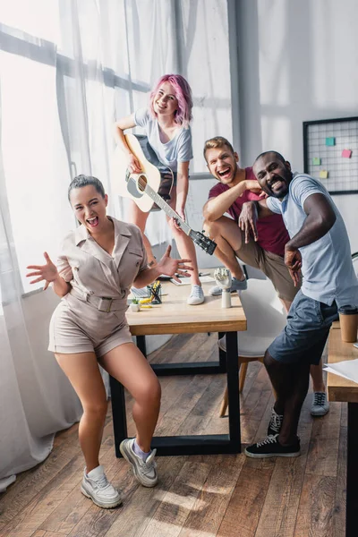 Selective focus of multiethnic business people dancing and playing acoustic guitar in office — Stock Photo
