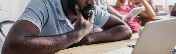 Récolte panoramique d'homme d'affaires afro-américain assis près d'un ordinateur portable sur une table de bureau — Photo de stock