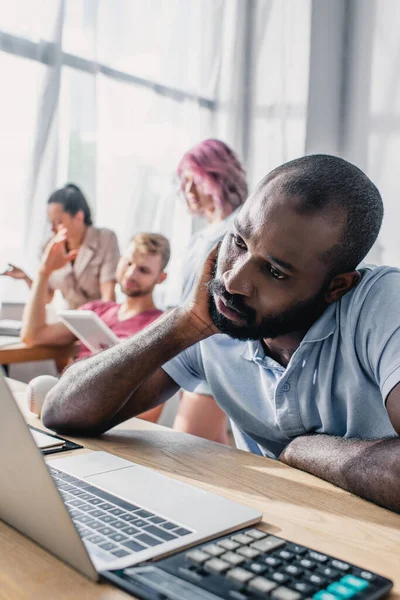 Selektiver Fokus eines afrikanisch-amerikanischen Geschäftsmannes, der Laptop betrachtet, während er in der Nähe multiethnischer Kollegen im Büro arbeitet — Stockfoto