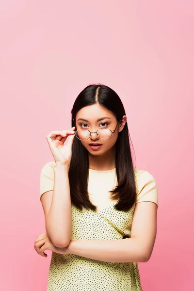 Attractive asian girl touching glasses isolated on pink — Stock Photo