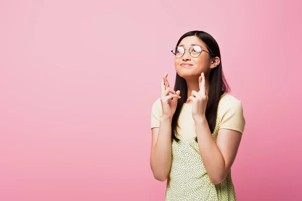 Young asian woman in glasses standing with crossed fingers isolated on pink — Stock Photo