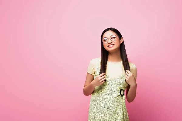 Fröhliche und junge asiatische Frau mit Brille lächelt auf rosa — Stockfoto