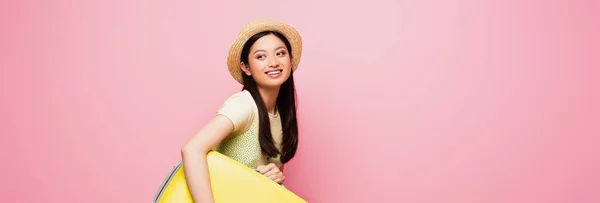 Sito web intestazione di allegra ragazza asiatica in cappello di paglia tenendo bagagli isolati su rosa — Foto stock