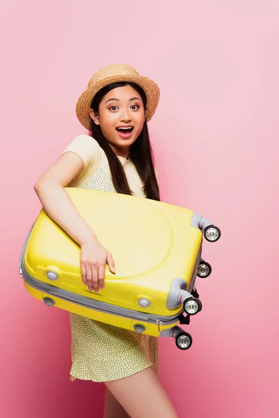 Aufgeregt asiatische Mädchen in Strohhut hält Gepäck auf rosa — Stockfoto