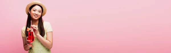 Панорамный урожай улыбающейся азиатки в соломенной шляпе, держащей стакан с коктейлем на розовом — стоковое фото