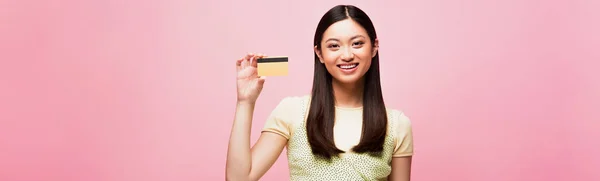 Récolte panoramique de sourire jeune asiatique femme tenant carte de crédit isolé sur rose — Photo de stock