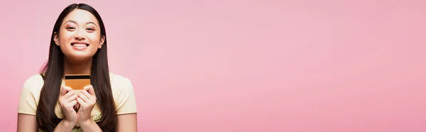 Horizontales Bild einer fröhlichen und jungen asiatischen Frau mit Kreditkarte isoliert auf rosa — Stockfoto