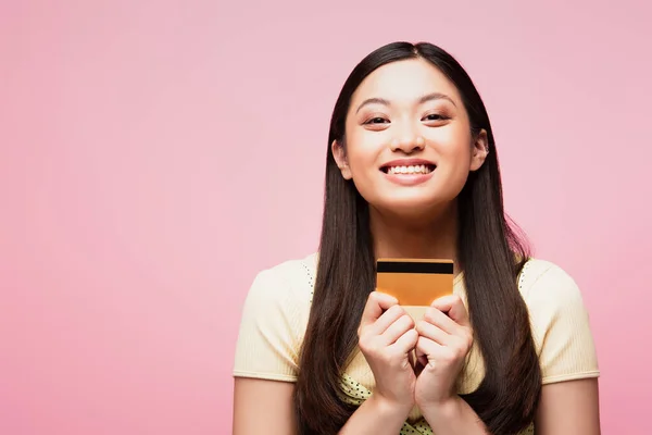 Allegro e giovane asiatico donna holding carta di credito isolato su rosa — Foto stock