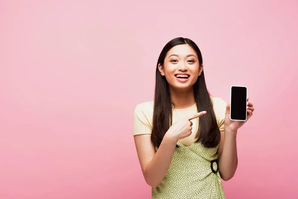 Positivo asiático mulher apontando com dedo para smartphone com tela em branco isolado no rosa — Fotografia de Stock