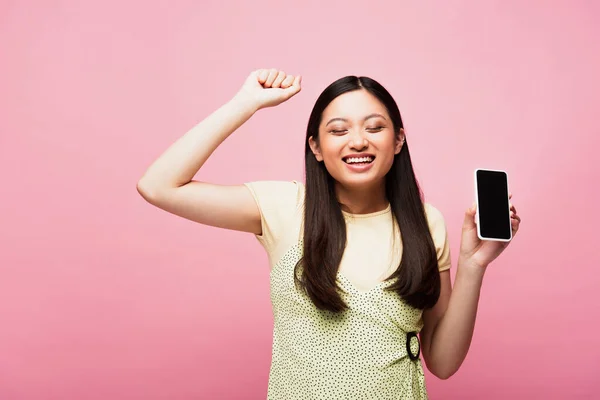 Positivo asiatico donna con chiuso gli occhi tenendo smartphone con vuoto schermo isolato su rosa — Foto stock