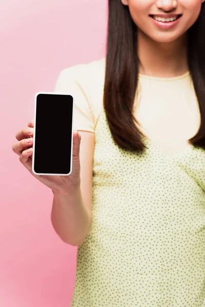Обрізаний вид позитивної жінки, що тримає смартфон з порожнім екраном ізольовано на рожевому — стокове фото