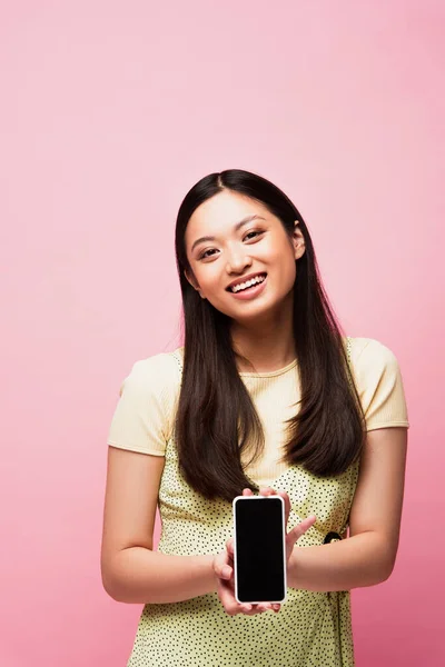 Счастливая азиатская женщина держит смартфон с чистым экраном изолированы на розовый — стоковое фото