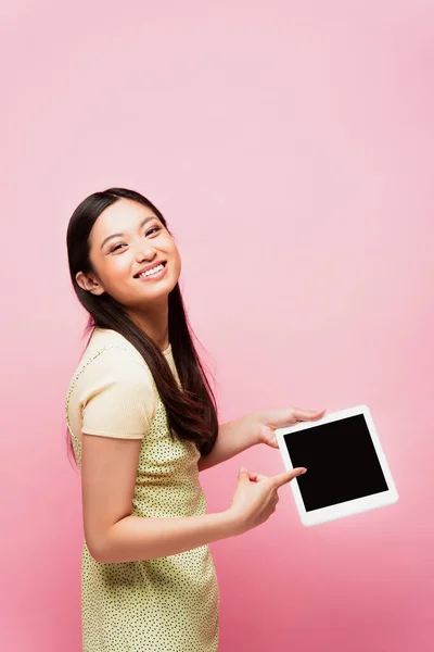 Cheerful asian woman pointing with finger at digital tablet with blank screen isolated on pink — Stock Photo