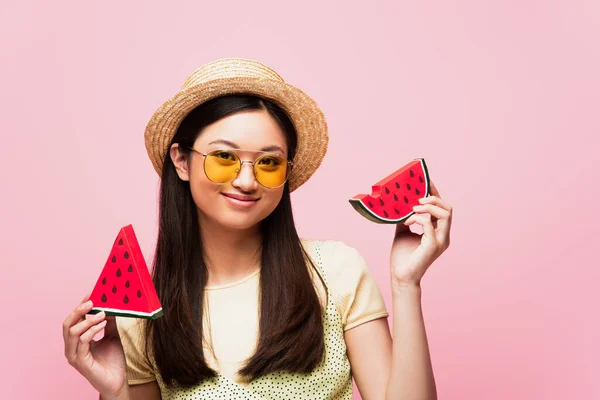 Feliz asiático mujer en gafas de sol y paja sombrero celebración en rodajas de papel sandía aislado en rosa - foto de stock